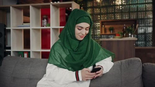 Woman with headscarf using mobile phone on couch