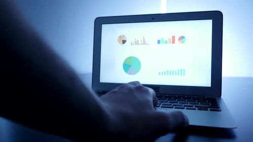 Typing on Laptop with Data Charts Displayed