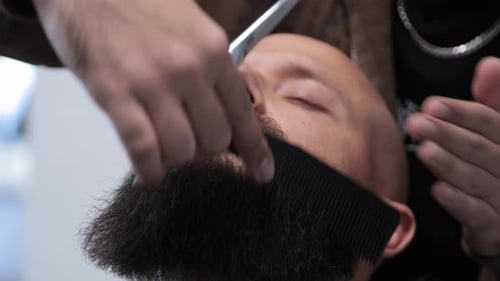 Close up of a moustache being combed by a barber. Young attractive bald man with long dark haired be