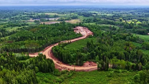 Curving Dirt Road Through Verdant Latvian Forest at Construction Site