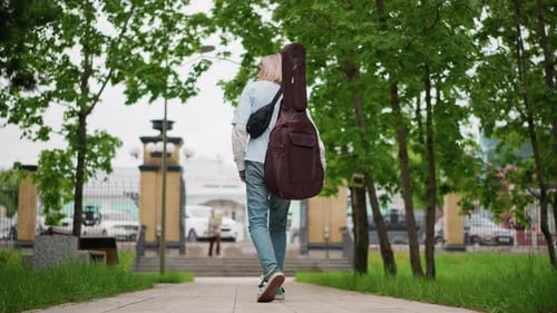 Guitarist Journeys Past Cityscape Street Performer Moves with Determined Pace Traveling Musician