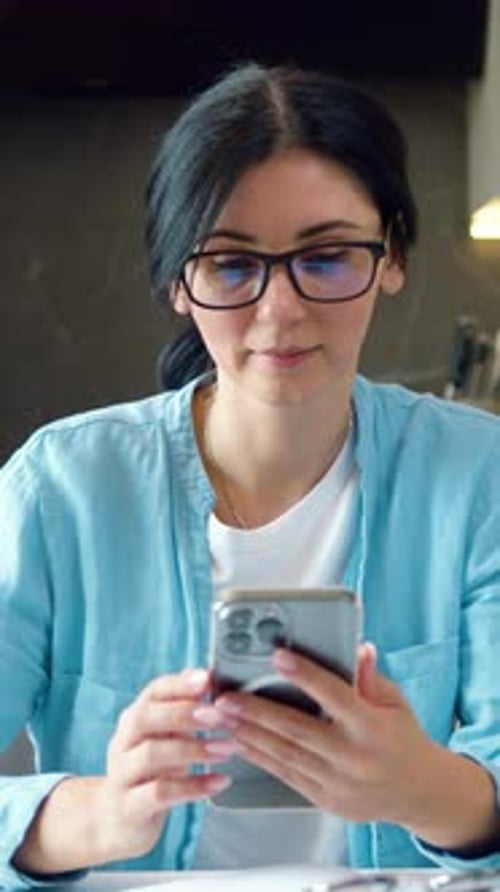 Woman with Glasses Working on Phone in Her Hand Messaging on Smartphone in Modern Home Office with
