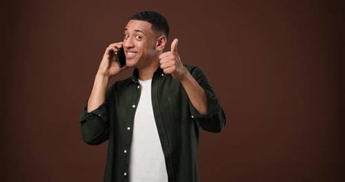 Young Serious African American Man Talking on the Phone Answering Phone Call Standing Over Brown