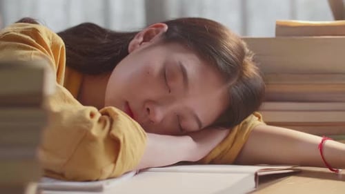 Close Up Of Young Asian Female Studying At Home Sleeping While Reading Books On The Table