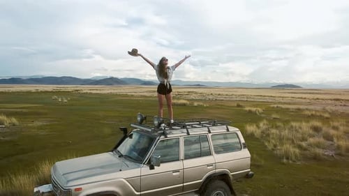 Young Woman Stands on SUV in Open Field