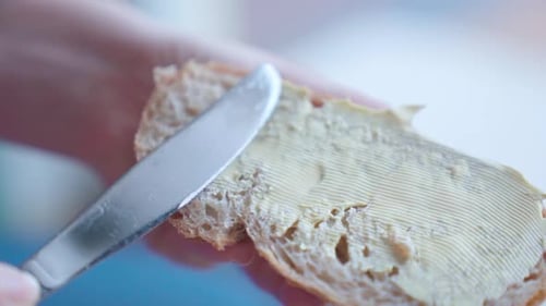 Close-up of a hand spreading butter on bread slice, soft focus, in slow motion