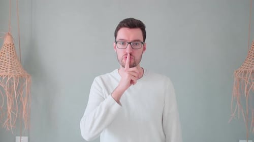 Junger Mann, Finger vor dem Mund, Zeichen der Ruhe, Verschwiegenheit, geheim halten, nicht erzählen, keinen Lärm machen