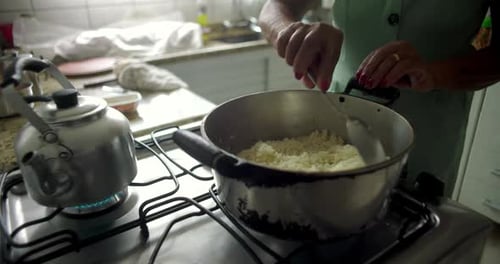 Close-up of a woman stirring rice in a pot on a stovetop, capturing the essence of home cooking,