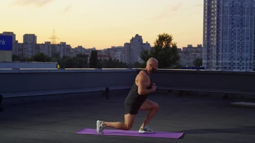Muscular Man Doing Leg Exercises on Rooftop at Sunset