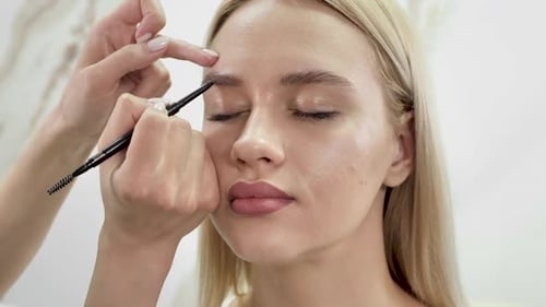 Stylist zeichnet Augenbrauen mit einem Bleistift für eine junge schöne Frau