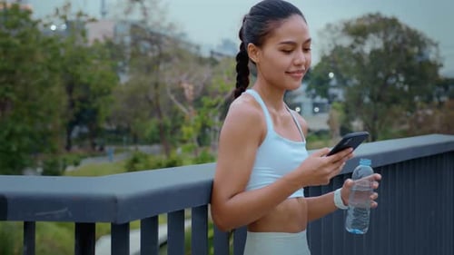 Woman Drinks Water, Uses Phone in Urban Park