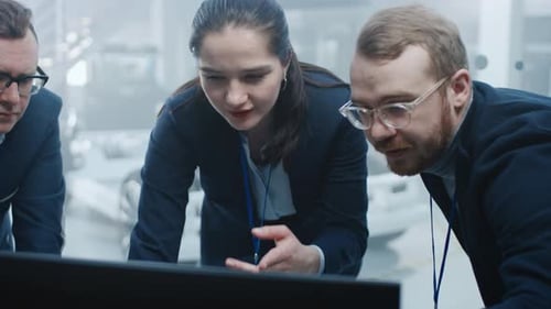 Automobilkonstrukteure arbeiten und diskutieren etwas auf einem Computerbildschirm neben einem El
