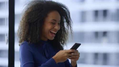 Excited African American Businesswoman Reading Good News Email Using Mobile Phone In Office. Moti...