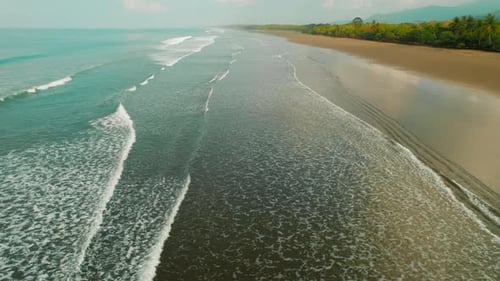 Long tropical beach with dark sand and calm ocean waves under sky in Costa Rica