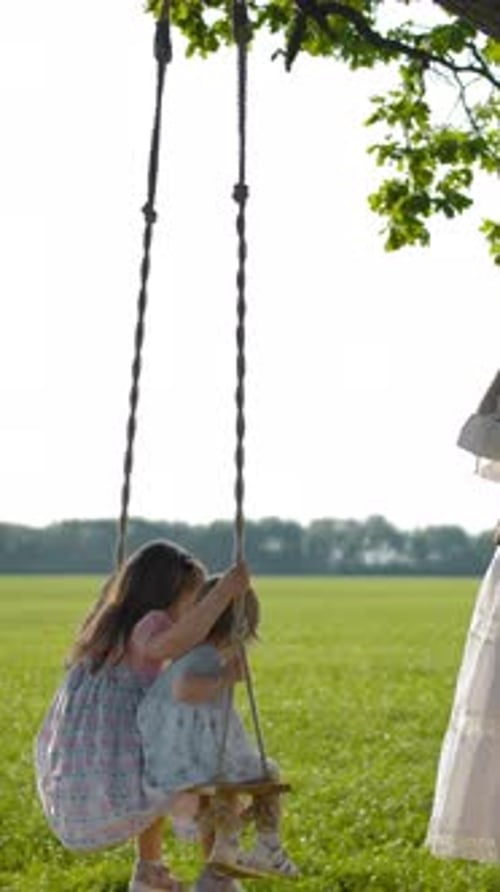 Mother and Daughters Swinging on a Sunny Day