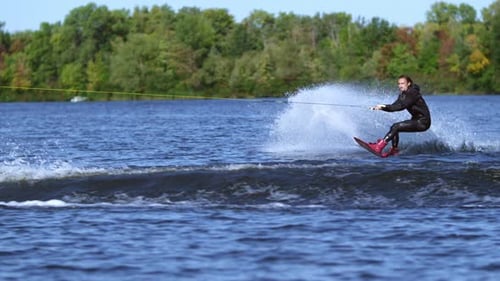 Wakeboarder jumps high above summer lake making dangerous trick in slow motion