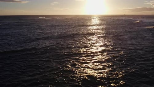 drone shot of the setting sun shining across the rippling ocean waves as the reflective rays follow