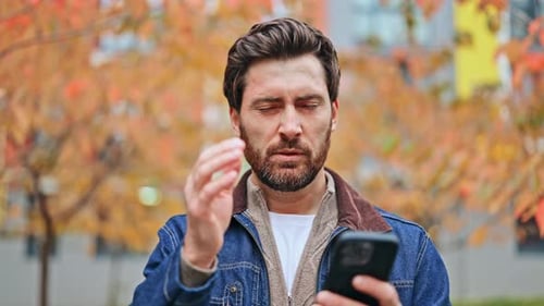 Stressed Man Experiences Headache Using Phone in Autumn