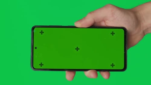 Male Hand Holding a Smartphone with Vertical Green Chroma Key Screen Isolated on Green Background