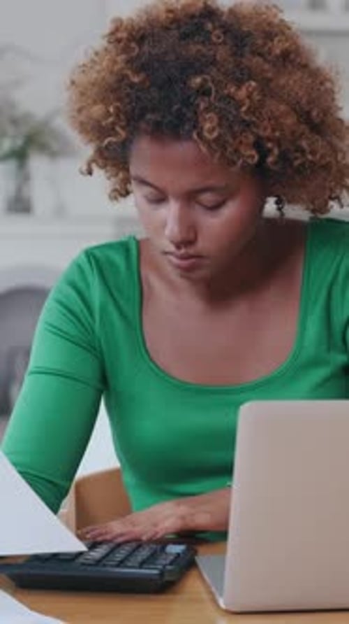 Young Woman Studies Documents While Working on Laptop at Home Desk