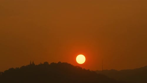 Time lapse of the sun setting over hills that are covered with clouds.