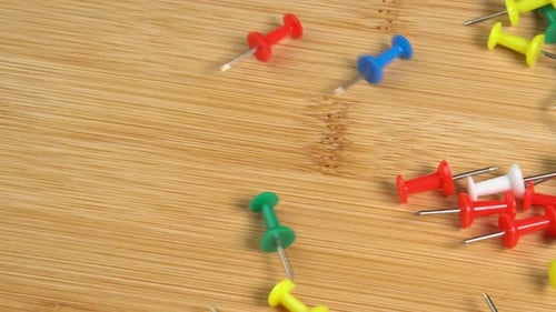 Colorful Push Pins Falling onto Wood Surface