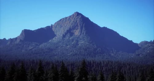 Majestic Mountain Peak Rises Above Dense Forest in Clear Blue Sky