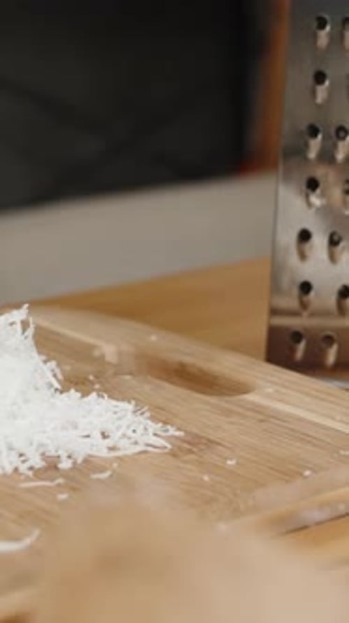 Vertical video. A Wooden Kitchen Table and Coconut Shavings Grated on a Metal Grater. Slider Shot.