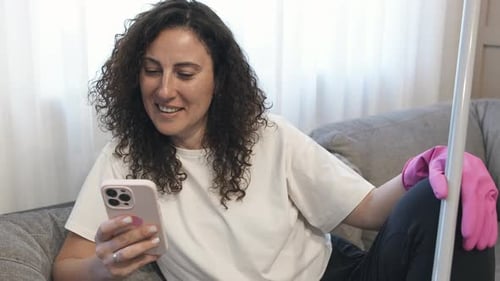 Beauty Curly Cleaning Woman in Pink Gloves Having Videocall Meeting on Phone Sitting on Sofa