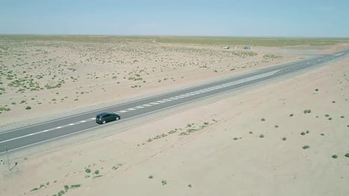 Aerial Panorama a Car Driving on a Highway Road Between Sands with Little Green Grass Bushes