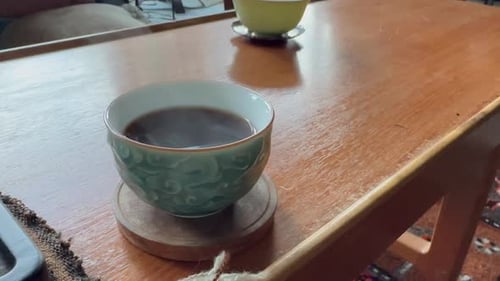 Dampf fließt über dunklen Tee in einer grün-weißen Keramiktasse.