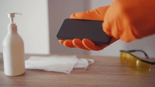Close Up Hands on Gloves Using Antiseptic and Disinfect Mobile Phone Screen Self Isolation at Home