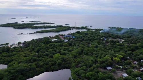 Isla tropical al atardecer mientras la gente local practica la quema de madera y rastrojos. Aéreo