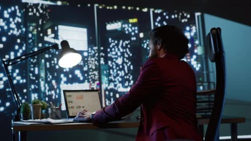 Adult Works Late at Desk Overlooking City