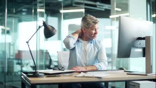 Man Rubbing Neck at Desk in Modern Office