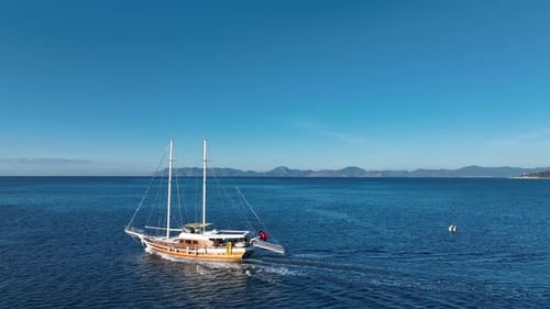Yacht auf ruhigen Gewässern: Eine Holzyacht schwimmt anmutig auf ruhigen Gewässern, eingerahmt von einer bergigen