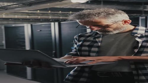 Man Working on Laptop in Front of Server