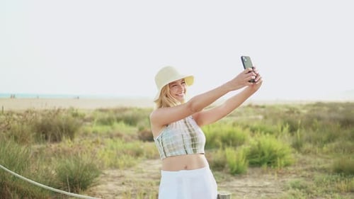 Young woman tourist takes a selfie with her mobile phone with the beach in the background on a sunny