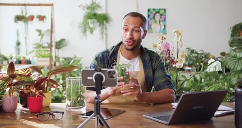 Jardinero, hombre afroamericano, bloguero, que usa el teléfono mientras cuida las plantas de interior y usa una pala