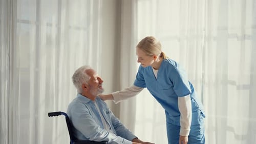 Friendly Nurse with Senior Man in Wheelchair Indoors
