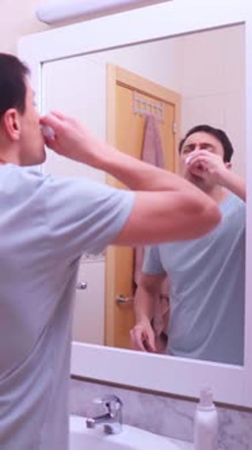 Man Using Mouthwash in His Bathroom Mirror