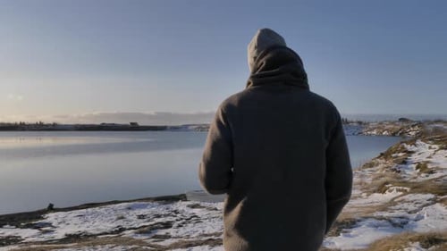 Follow shot of young male travel walking at scenic lake while drinking coffee