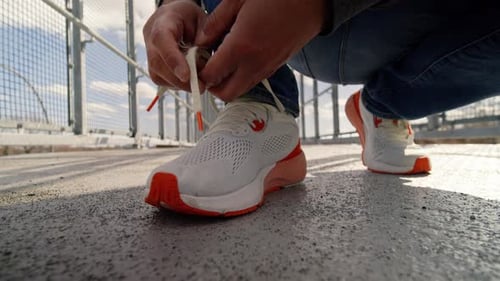 Man Prepares For Urban Walk At Sunset Lacing White Sneakers Outdoors