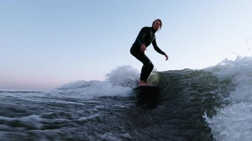 A Skilled Surfer Navigates Ocean Waves During Sunset Showcasing Perfect Balance and Technique on a