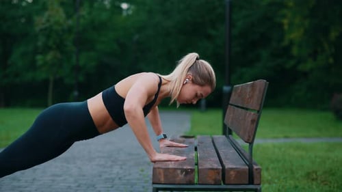 Mujer atleta caucásica entrenando en el banco haciendo flexiones usando auriculares escuchando música