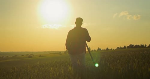 Back View of the Young Farmer Standing at the Field with Shovel and Looking at the Harvest While