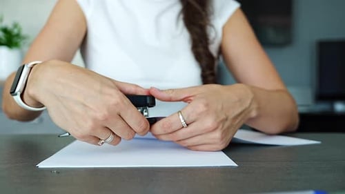 Close Up of Woman Hands Stapling Documents with Stapler on Desk in Home Office Paperwork