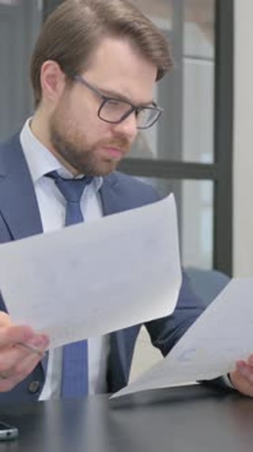 Man in Suit Reviews Documents at Desk