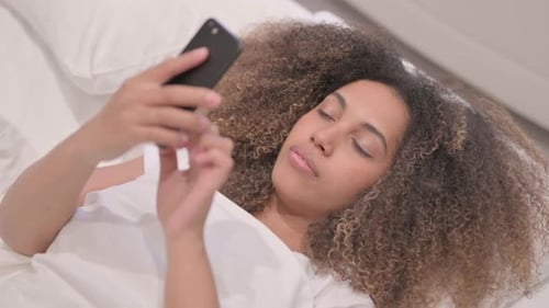 African American Woman using Smartphone while Lying in Bed