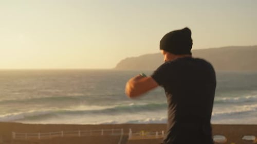 Athletic Man with Dumbbells Throwing Punches in Air Near Sea